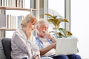 Caucasian man and a woman using laptop on a cozy sofa at home, Retired elderly family reading documents, Senior couple checking