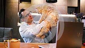 Caucasian man working on laptop with cat in home office. male freelancer working on computer in kitchen.