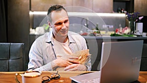 Caucasian man working on laptop with cat in home office. male freelancer working on computer in kitchen.