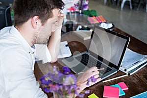 Caucasian man working on laptop while sitting at his modern office place. Concept of young people using coworking place.