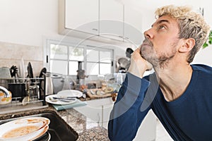 Caucasian man worried about the mess of dirty dished and rubbish in his kitchen in the morning