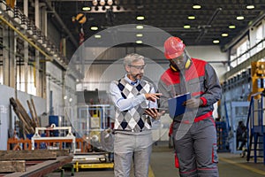 Caucasian Manager Giving Orders To Black Worker in Protective Workwear With Clipboard