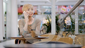 Caucasian mature adult middle aged 40s woman business lady sitting at table in cafe talking on mobile phone smartphone