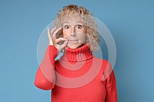 Caucasian mature woman shutting mouth and lips shut as zip with fingers.