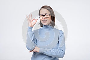 Caucasian mature woman with wide smile wearing glasses showing ok symbol with fingers.