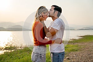 Caucasian man kiss on forehead of beautiful woman with sunset light near lake and look romantic for couple love stay together