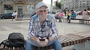 Caucasian middle-aged man sitting on a bench writes an SMS message
