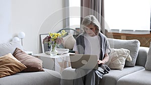 caucasian Middle aged older woman working on laptop at home sitting on sofa