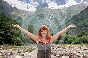 Caucasian middle aged woman holding arms up showing happiness being in valley between mountains