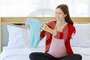 Caucasian millennial young happy female prenatal pregnant mother in casual pregnancy outfit jacket sitting smiling on bed in