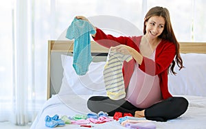 Caucasian millennial young happy female prenatal pregnant mother in casual pregnancy outfit jacket sitting smiling on bed in