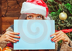 Caucasian Model Female in a Santa Hat Covered the Lower Part of her Face with a Bluish Sheet of Paper, has Pen in her