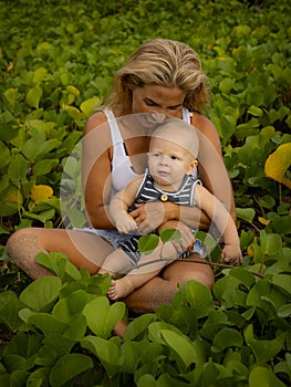 Caucasian mother with baby infant boy spending time in nature. Outdoor activities. Mum and baby boy sitting on the ground. Summer