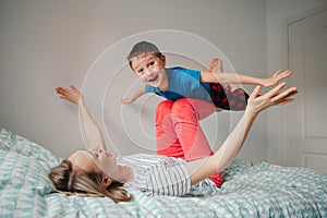 Caucasian mother and boy son playing in bedroom at home. Mom rocking child on her knees feet legs. Family having fun together.