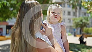 Caucasian mother concentrates on smartphone talk, standing and holding her little daughter in arms, seriously calling at park