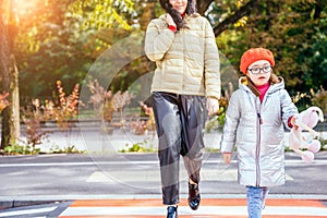 Caucasian mother crossing street and commuting downtown city with little daughter wearing eyeglasses and red beret hold