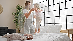 Caucasian mother and daughter bonding, jumping on the bed together, smiling inside their cozy bedroom, waking up a happy home with