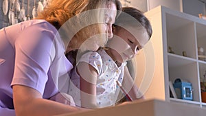 Caucasian mother doing homework with her daughter, helping kid with study, sitting at modern home, family concept