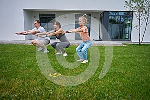 Caucasian mother, father and daughter doing sit ups on green grass in yard