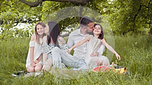 Caucasian mother and father kissing and embracing their two little daughters during summer picnic on nature. Concept of