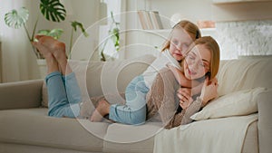 Caucasian mother in glasses lying on couch sofa in home living room little cute daughter kid child baby girl embrace hug