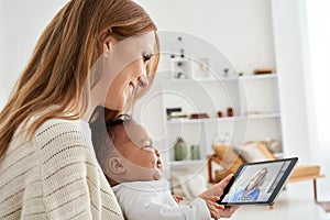 Caucasian mother holding crying african baby having meeting video call at home.