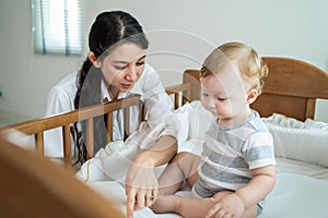 Caucasian mother play with cute baby boy child on infant bed at home. Happy family, attractive young woman mom read book to