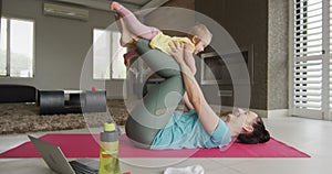 Caucasian mother playing with her baby while practicing yoga on yoga mat at home