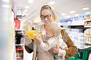 Caucasian mother shopping with her infant baby boy child choosing products in department of supermarket grocery store.