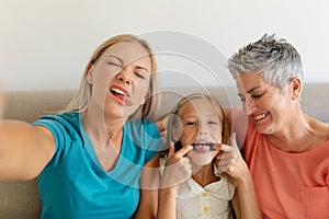 Caucasian mother sitting on couch taking selfie making faces with daughter and grandmother