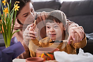 Caucasian mother teaching her little child with down syndrome to replacing flowers to the pots