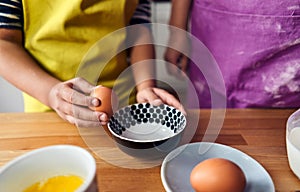 Caucasian mother teaching her son to cook and preparing the ingredients to make a cake. Child breaking an egg