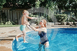 Caucasian mother training toddler son to swim in swimming pool outdoor. Baby boy diving jumping in water with goggles. Water