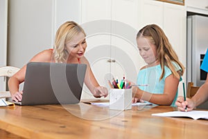 Caucasian mother using laptop and doing homework with her daughter smiling at home