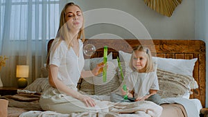 Caucasian mother woman mom with small little child girl kid baby adopted healthy daughter blowing soap bubbles in air in