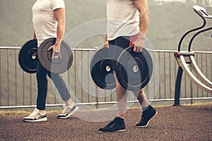 Caucasian muscular men with weight plates preparing to outdoor workout.