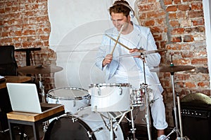 Caucasian musician playing drumms during online concert with the band at home isolated and attented, smiling, cheerful