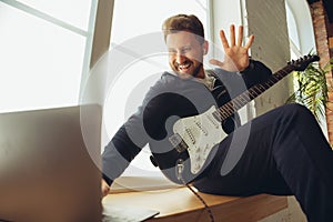 Caucasian musician playing guitar during concert at home isolated and quarantined, cheerful improvising with the band