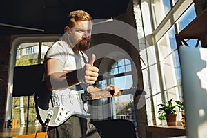 Caucasian musician playing guitar during online concert at home isolated and quarantined, thumb up, nice