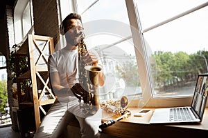 Caucasian musician playing saxophone during concert at home  and quarantined, impressive improvising with band photo