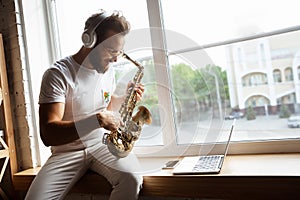 Caucasian musician playing saxophone during online concert at home  and quarantined, impressive improvising photo