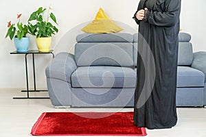 A caucasian Muslim woman in a traditional black abaya and hijab prays Salat. No face