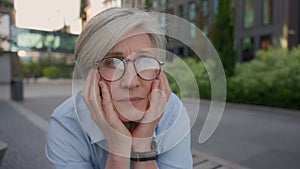 Caucasian old business woman senior middle age female sorrowful thoughtful 50s lady in eyeglasses sit outdoors looking