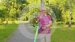 Caucasian old gray-haired senior stylish man grandfather riding electric scooter in summer park