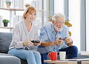 Caucasian old senior elderly lovely happy grandparents married couple husband and wife sitting playing competition on console