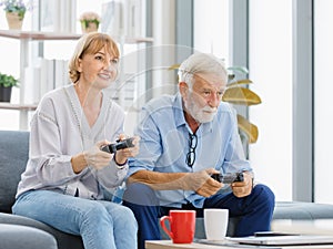 Caucasian old senior elderly lovely happy grandparents married couple husband and wife sitting playing competition on console