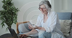 Caucasian older woman in eyewear using a credit card and a laptop to purchase online.