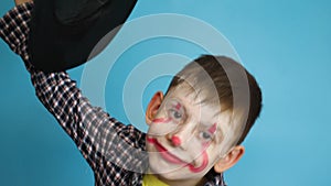 Caucasian peppy child 8 years old painted face with makeup in a hat for the Halloween holiday.Child scares with a painted clown ma