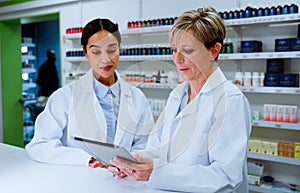 Caucasian pharmacist manager helping mixed race assistant using digital tablet standing in pharmacy drugstore