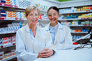Caucasian pharmacist manager and mixed race female assistant smiling while standing in pharmacy